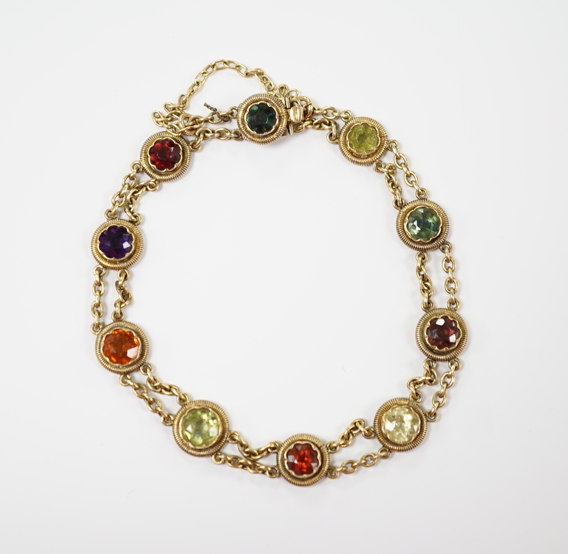 An early 20th century yellow metal (stamped 15 and also 9??) and ten stone multi gem set chain link bracelet, 16cm, gross weight 14.6 grams, the stones include amethyst, hessonite garnet and tourmaline.